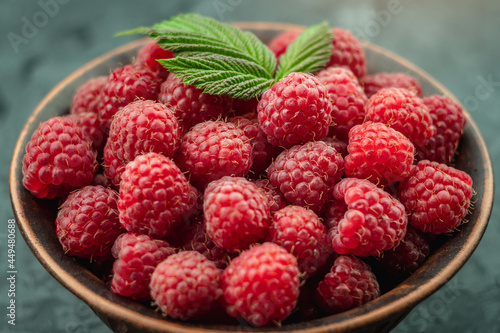 Bowl with fresh ripe delicious raspberries and a green leaves on a black background