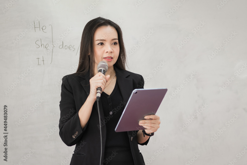Stock photo portrait of a confident cheerful Asian woman teacher in a black business suit uniform with a digital tablet and laptop to teach modern language in the classroom Stock photo portrait of a confident cheerful Asian woman teacher in a black business suit uniform with a digital tablet and laptop to teach modern language in the classroom
