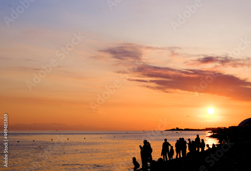 group of happy people and their silhouettes that are on the beach against the sunset. Beautiful landscape of the ocean or the sea