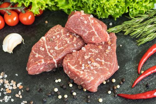 Raw fresh marbled beef meat, seasonings on dark stone cutting board