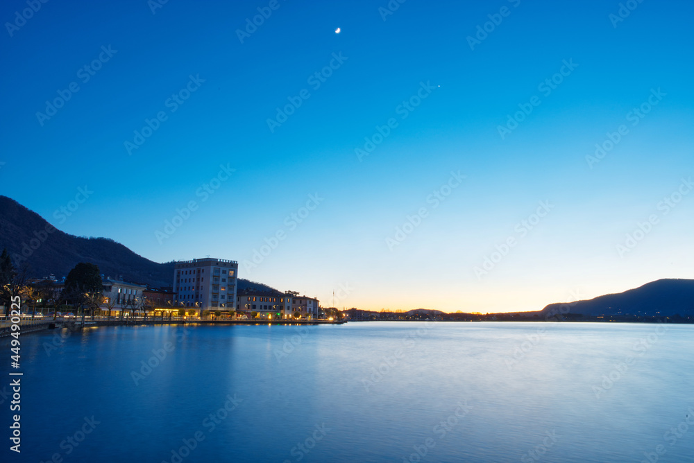 In evening, under the blue sky, the lights of a village near the ocean are lit In evening, under the blue sky, the lights of a village near the ocean are lit