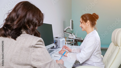 Woman doctor in white uniform types information on computer keyboard listening to female patient in hospital office at appointment close view