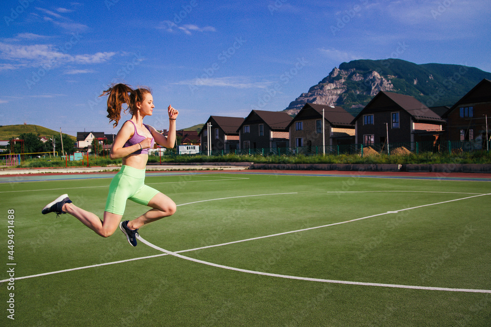 A young woman jumps on a football field. A girl at the stadium is engaged in sports.A healthy lifestyle.