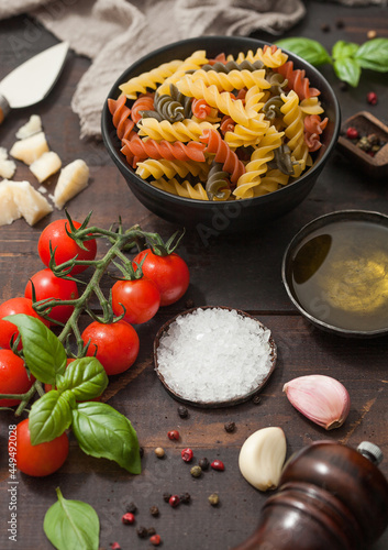 Fusilli tricolor pasta with parmesan and tomatoes, parmesan cheese and tomatoes on wooden background with salt and pepper