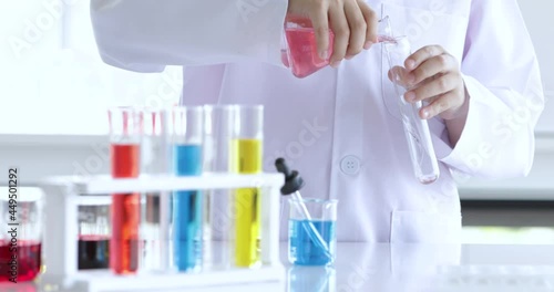 Young little primary schoolboy wearing doctor gowns dress trying to mix the colorful liquid solution and watch the result with concentrate and focus.  Concept of schoolboy learning and studying.