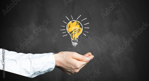 female hands with a lightbulb symbol in front of a chalkboard