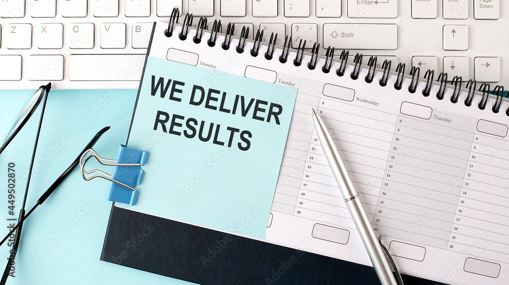 WE DELIVER RESULTS text on blue sticker on the planning and keyboard,blue background