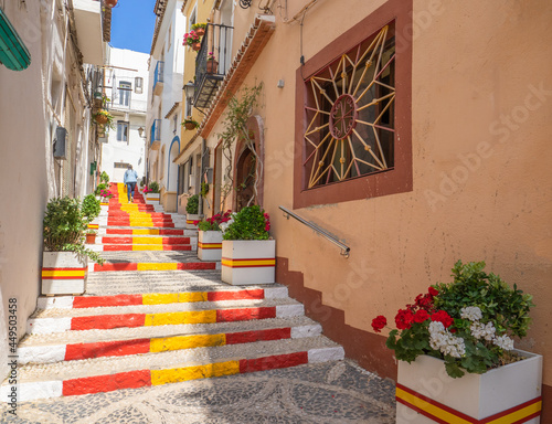 Fototapeta Naklejka Na Ścianę i Meble -  Calle Puchalt is a bright and narrow alley in the center of Calpe with the staircase painted in the colors of the Spanish flag.Costa Blanca, Spain
