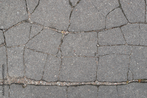 An old asphalt road surface with a surface torn by chaotic narrow cracks and wrinkles filled with small pebbles. Vintage, grunge abstract design background.