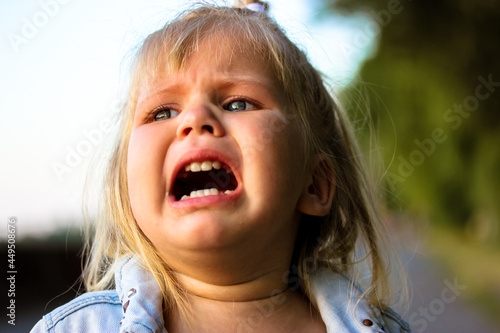 Cute blonde infant girl is crying on a street. Upset kid. Child psychology.
