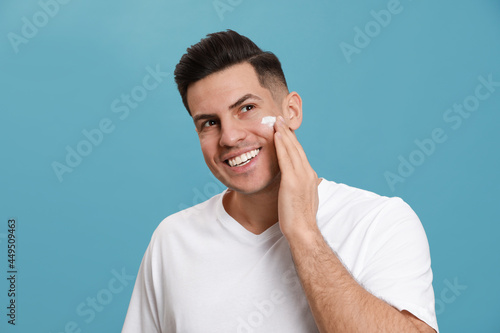 Happy handsome man applying face cream against turquoise background