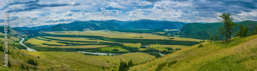 Panoramic view of plain with river near hills and mountains under white fluffy clouds in blue sky at sunny day © photollurg