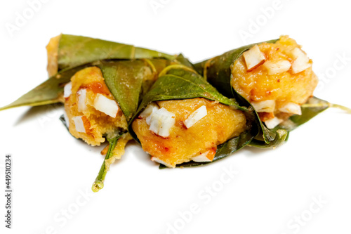 Traditional steamed ripe palmyra palm fruit cake wrapped with jackfruit leaves and sprinkled with coconut pieces. Steamed palmyra palm cake in isolated white background. photo