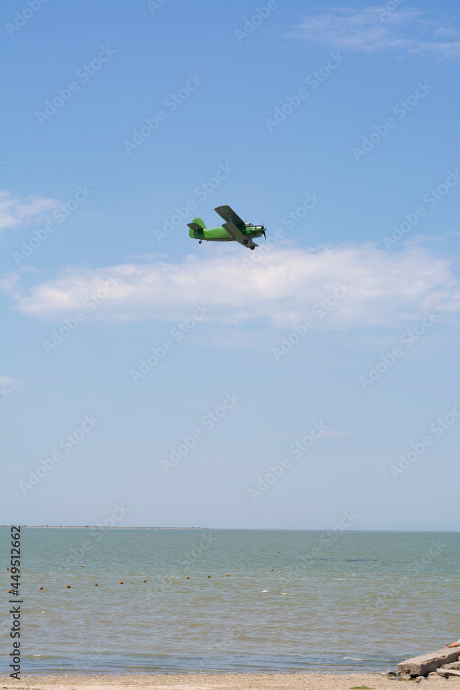 Fototapeta premium Old green retro plane flies in the blue sky over the sea on a summer day, background, place for text.
