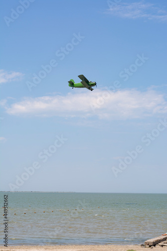 Old green retro plane flies in the blue sky over the sea on a summer day, background, place for text.