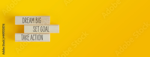 Banner con frase motivazionale scritta su piccoli assi di legno poggiati su sfondo giallo. Dream big, set goal, take action. photo