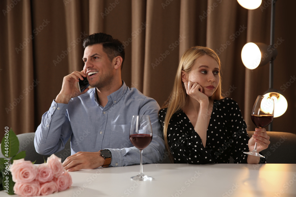 Man talking on phone instead of spending time with young woman during first date in restaurant - obrazy, fototapety, plakaty 