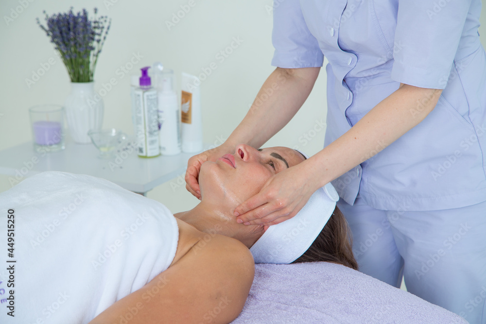 Obraz premium A girl doctor in a lavender-colored suit performs a very beautiful and professional massage of the face of a girl lying on a couch