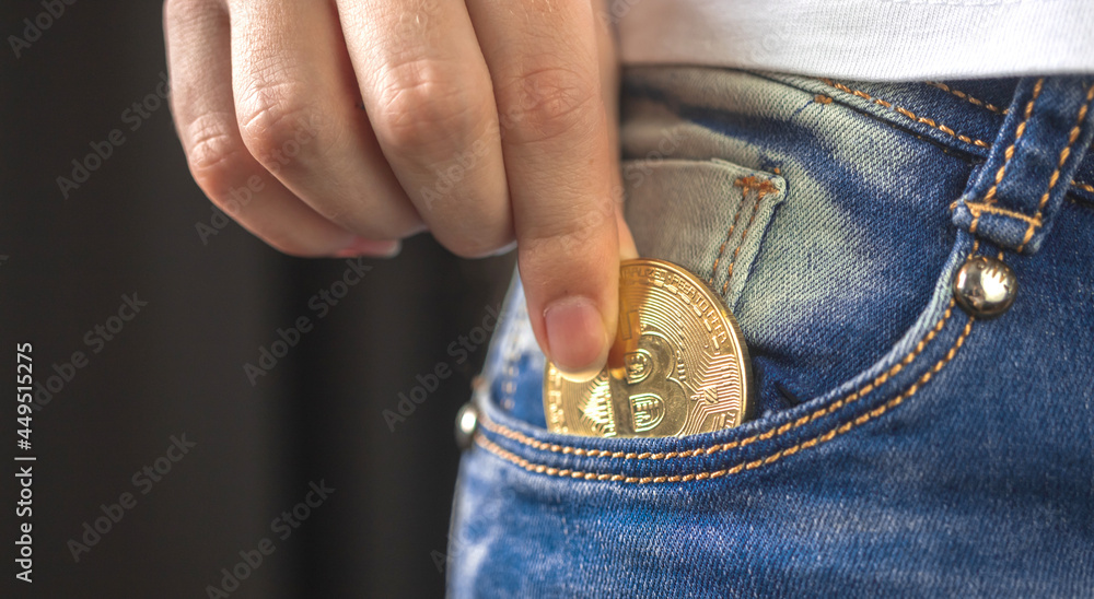Fototapeta premium Banner woman putting bitcoin in jeans pocket, golden cryptocurrency coin in pocket background photo