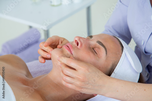 A girl doctor in a lavender-colored suit performs a very beautiful and professional massage of the face of a girl lying on a couch