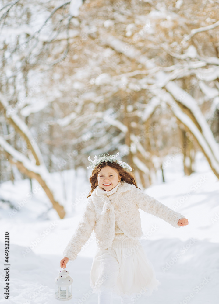 Happy little girl runs on a forest path with a lantern in her hand. Christmas time. Sunny winter day. Happy little girl runs on a forest path with a lantern in her hand. Christmas time. Sunny winter day.