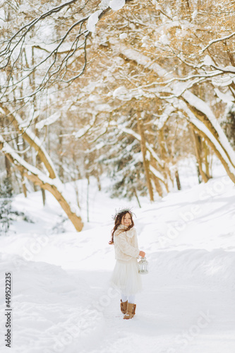 Fabulous girl walks on a forest path with a lantern in hand. Christmas time. Sunny winter day. © Yuliia