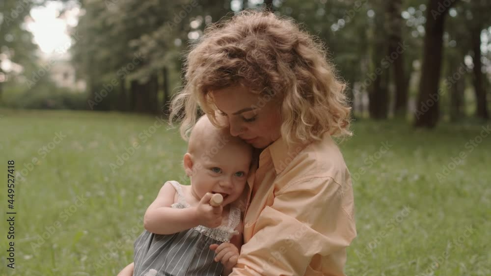 Medium close-up of beautiful young woman and her cute toddler daughter in pretty summer dress spending time together outdoors in park Medium close-up of beautiful young woman and her cute toddler daughter in pretty summer dress spending time together outdoors in park
