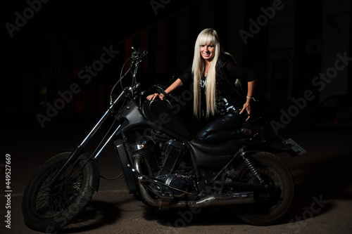 Sexy biker girl is posing on motorcycle in the night. She is happy looking at camera.