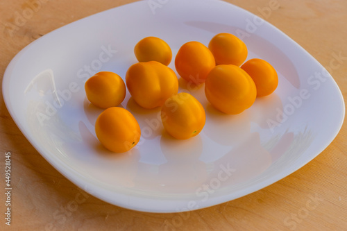 Fresh yellow caramel tomatoes on a white glossy plate. Side view