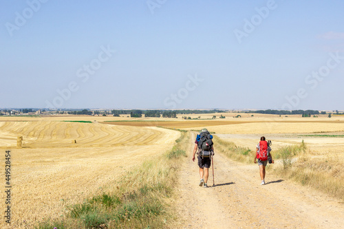 people walking in a hike with backpacks on their backs on dirt road towards the nearest town unrecognizable