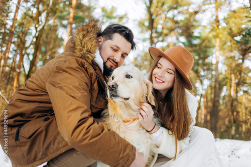 Family outdoors. Romantic lovely woman and brutal man in winter forest having a leisure time with golden retriever dog.