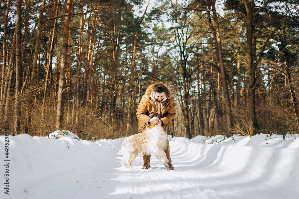 A man plays with a dog in the winter forest.