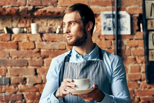 male waiter in apron with a cup of hot drink brick wall in the background