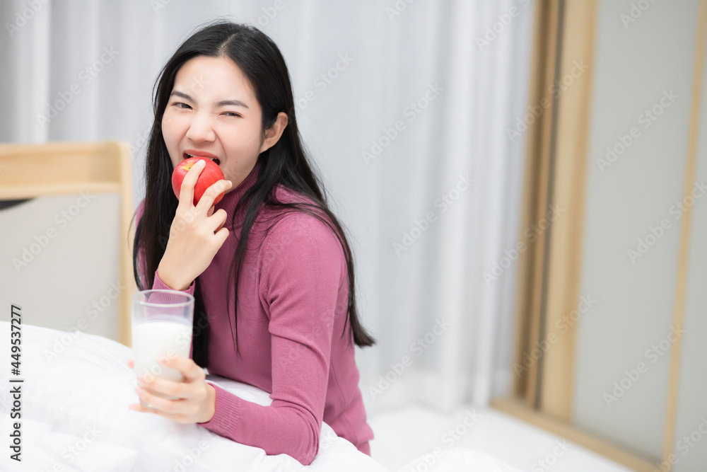 Beautiful Asian Thai woman sitting in bed enjoying eating apples and drinking milk.