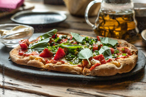 Roman pizza margarita with pesto sauce and basil. Side view on a black plate. Wooden background.