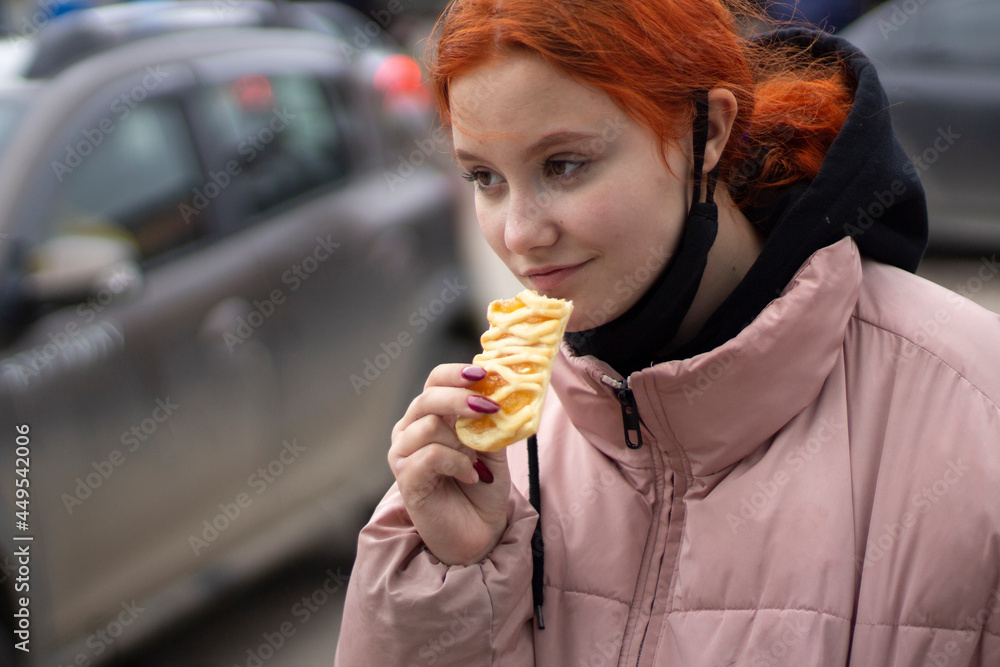 The girl eats flour. The girl is eating a sweet cake on the street.
