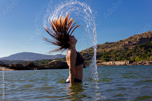Young woman in a bikini doing a wave with her hair in a lake. Summer. Movement concept. Copy space. Selective focus. © Rodrigo