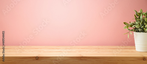 Empty wooden table with home plant decor over pink wall background. Interior mock up for design and product display.