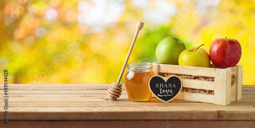 Jewish holiday Rosh Hashana concept with honey jar and apples on wooden table over nature bokeh background photo