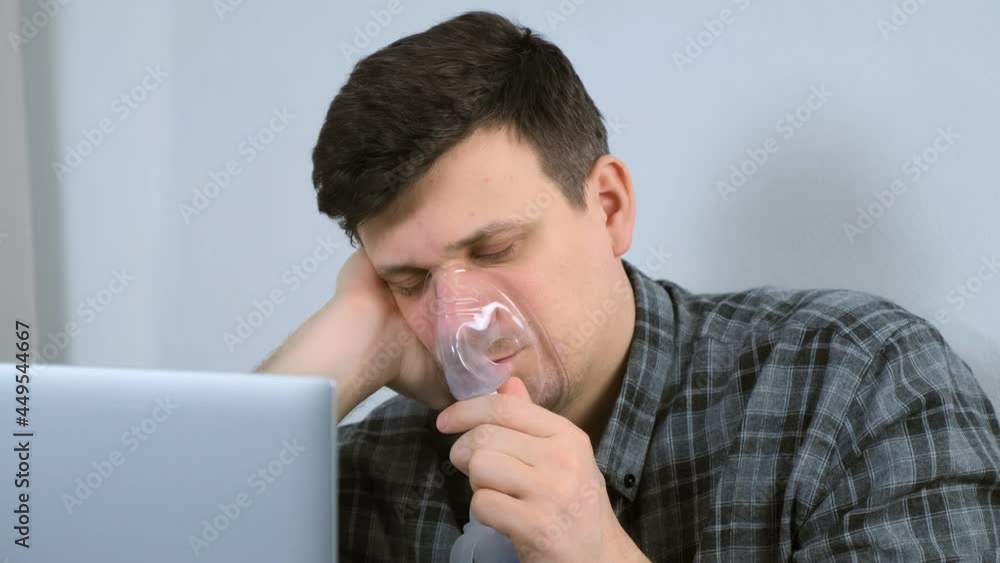 Portrait of sick young man is using nebulizer and inhaler for treatment at home and working on laptop. He is breathing in mask. Fibrosis, covid-19, asthma copd. Treatment, cure and procedure, therapy. Portrait of sick young man is using nebulizer and inhaler for treatment at home and working on laptop. He is breathing in mask. Fibrosis, covid-19, asthma copd. Treatment, cure and procedure, therapy.