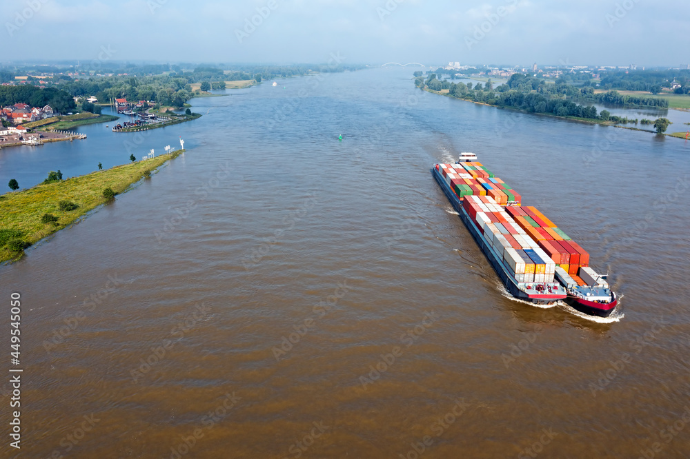 Obraz premium Aerial from a freighter full of containers cruising on the river Merwede near Gorinchem in the Netherlands in a flooded landscape