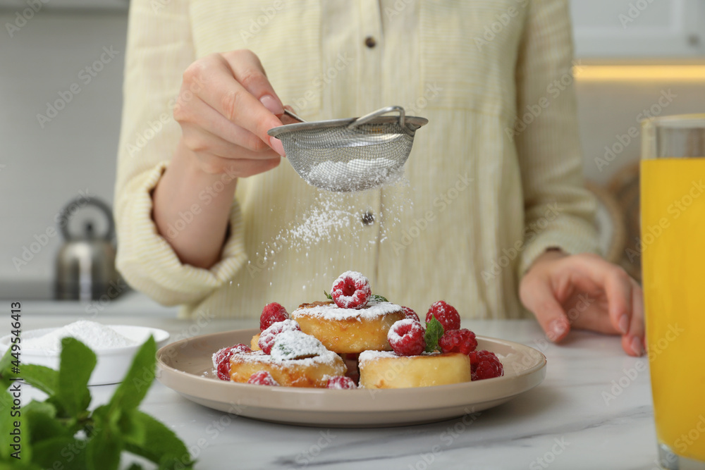 Woman sieving powdered sugar on cottage cheese pancakes at white table, closeup