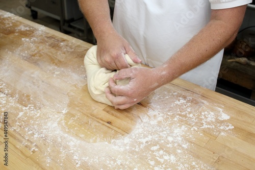 Closeup of baker kneading dough on wooden table