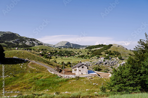 Panorama of a house by the road in a high-mountain village among trees, grasses and greenery