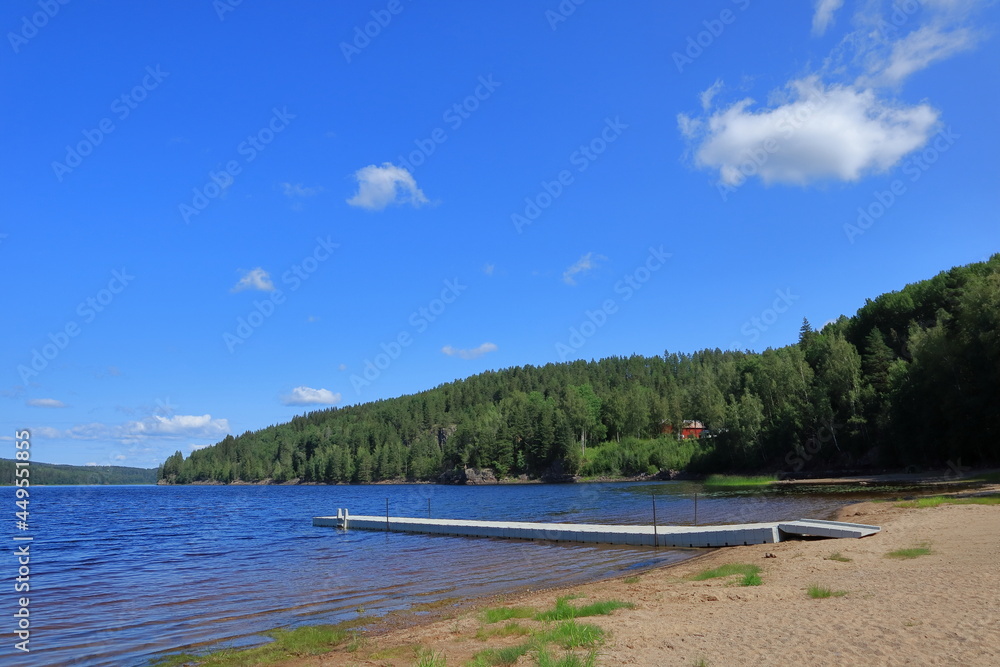 One typical Swedish beach during the summer. Sand, water, bridge and some trees in the background. Copy space for text. Värmland, Sweden, Europe.