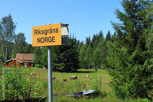 Border sign to Norway. View from the Swedish side. Summer photo during the month of July year 2021. Green nature, some sheep and a red house. Nice nature a sunny day. Värmland, Sweden, Europe.