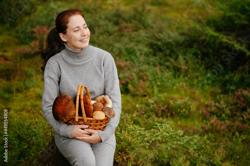 Woman is resting in a green forest with bascket of mushrooms. Concept of ecotourism.