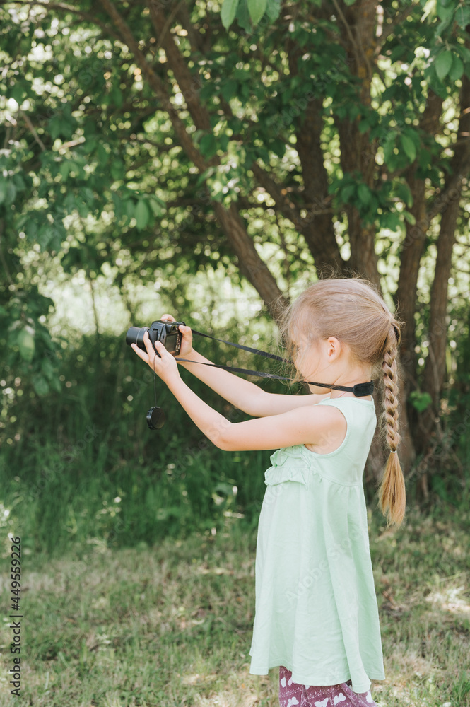 a happy little seven year old kid girl photographs a summer natural landscape with a camera using live view. children adopt their parents hobbies. summer children's education on vacation