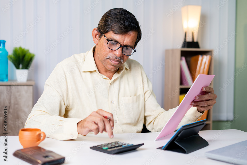 Businessman checking or verifying bills, expenses or taxes and calculating be seeing bills and calculator at office - concept of managing budget and financial work. Businessman checking or verifying bills, expenses or taxes and calculating be seeing bills and calculator at office - concept of managing budget and financial work.
