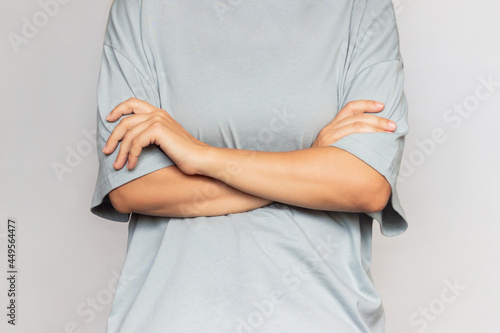 A cropped shot of a young woman crossing her arms on her stomach on a gray background. Closed pose © Марина Демешко